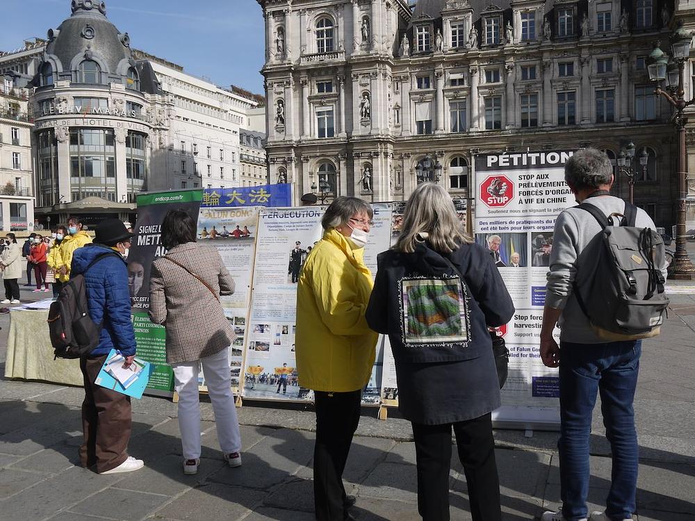 Ljudi čitaju plakate na trgu ispred Gradske vijećnice i postavljaju pitanja o Falun Gongu