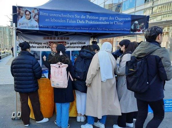 Prolaznici se zaustavljaju kako bi dobili informacije na Falun Dafa štandu u Düsseldorfu 5. marta 2022. i potpisuju peticiju za osudu progona.
