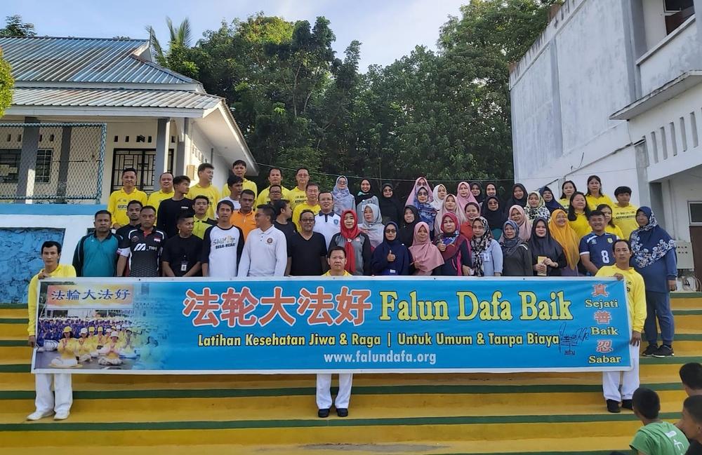 Grupna fotografija Falun Dafa praktikanata s upravnicom škole (u sredini, drugi red osoba s crvenom maramom), zamjenicom upravnice (prva s desna, drugi red) i nastavnicima. Indonežanska fraza ispisana na transparentu znače: „Falun Dafa Baik” (Falun Dafa je dobar), „Latihan Kesehatan Jiwa & Raga” (Vježbe za zdravlje uma i tijela) i „Untuk Umum & Tanpa Biaya” (Otvoreno za javnost i besplatno).