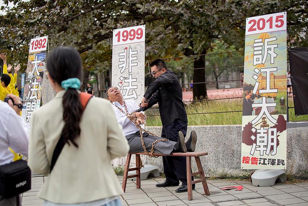 Prolaznici gledaju insceniranje metoda mučenja koje se koriste u progonu Falun Gonga.