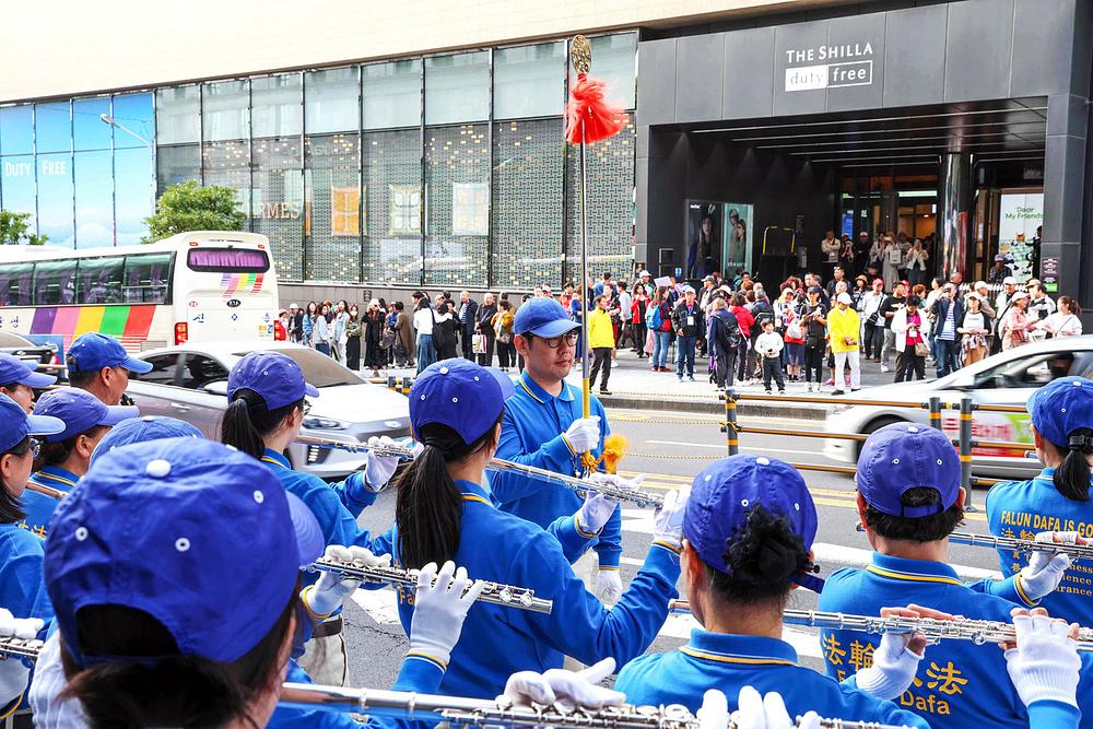  Turisti prate nastup Tian Guo Marching Banda ispred Shilla Duty-Free centra.
