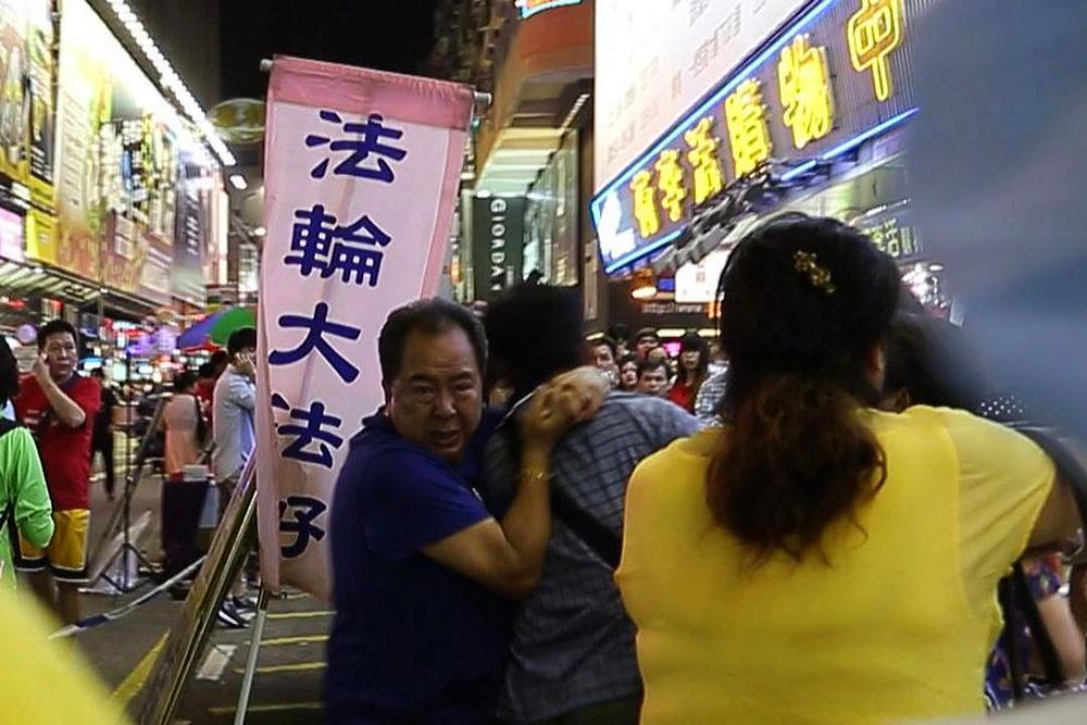 Lin Guo-an (u plavoj majici na lijevoj strani), potpredsjednik HKYCA, je zgrabio posmatrača za vrat dok ga je drugi član YCA, Xiao Xiaorong, udarao nogama. Ovo se desilo 14. jula 2013. godine, nakon što je posmatrač optužio policajca zaduženog za tu lokaciju da je propustio primijeniti zakon da bi zaštitio praktikante Falun Gonga.