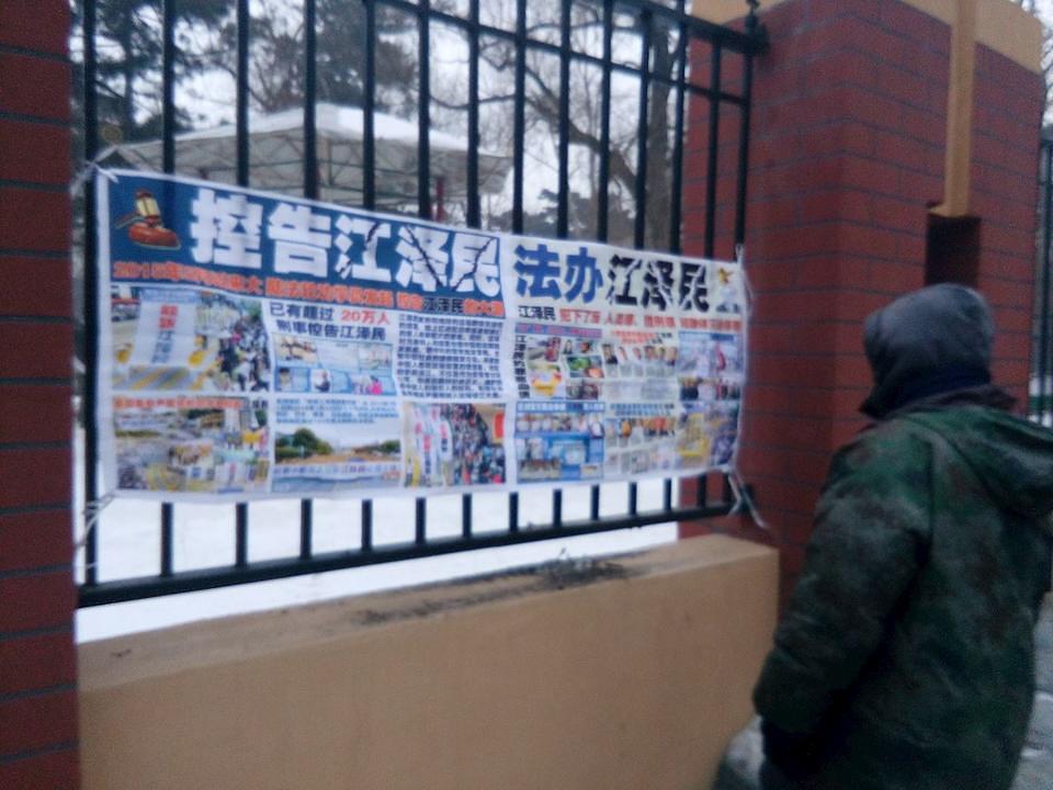 Prolaznici u gradu Changcunu u provinciji Jilin čitaju postere o privođenju pred lice pravde bivšeg kineskog vođe Jiang Zemina zbog proganjanja Falun Dafa.