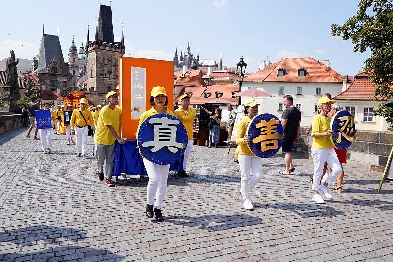 Tri praktikantice drže tri kineska znaka Istinitost-Dobrodušnost-Tolerancija, što su principi Falun Dafa. Iza njih dva praktikanta drže ogroman model glavne knjige Falun Dafe, *Zhuan Falun*, dok se povorka probija povijesnim Karlovim mostom 